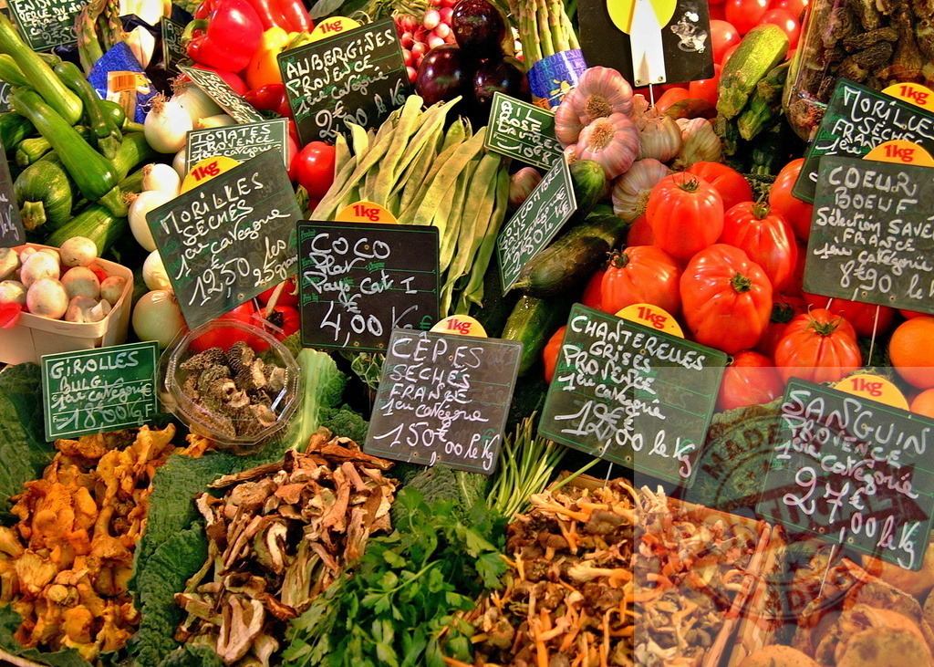 French market stall displaying fresh organic produce and mushrooms | French market stall offering a variety of colorful fresh vegetables, mushrooms, and fruits with chalkboard signs - Realized with Pictrs.com