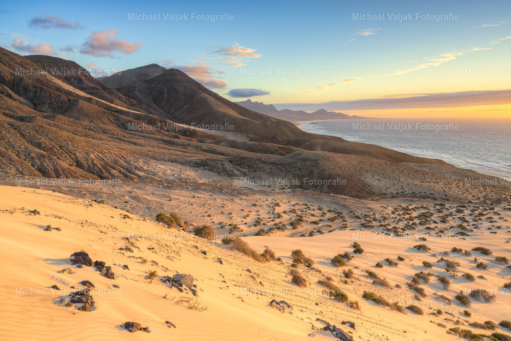 Jandia Fuerteventura | Von den Dünen in Jandía öffnet sich der Blick weit über die Landschaft bis zu den südlichen Bergen. Das Licht liegt weich über dem Sand, die Formen der Dünen laufen ruhig in die Ferne und treffen dort auf die dunkleren Silhouetten der Berge. Die Szene wirkt klar, weit und unaufgeregt – ein Moment, in dem Fuerteventura seine stille, natürliche Schönheit zeigt. - Realisiert mit Pictrs.com