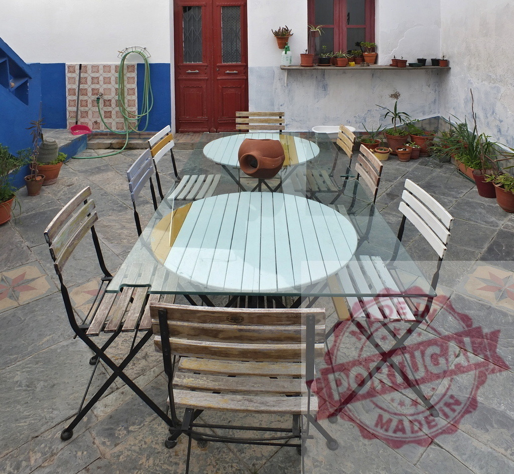 Courtyard patio with glass table and wooden chairs | Outdoor patio featuring a glass-top table, wooden chairs, terracotta pot, and blue wall in a garden setting - Realisiert mit Pictrs.com