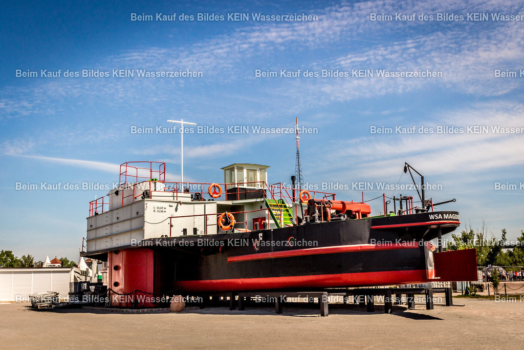 Magdeburg Tauchschiff-9453 | Das Foto zeigt den Taucherschacht II im Wissenschaftshafen Magdeburg aus einer bodennahen Perspektive. Die zylindrische Stahlkonstruktion mit ihren genieteten Bauteilen vermittelt einen eindrucksvollen Eindruck der Ingenieurtechnik des frühen 20. Jahrhunderts. Durch die niedrige Kameraposition werden die massiven Abmessungen und die technischen Details des Bauwerks besonders wirkungsvoll hervorgehoben.Der Taucherschacht II wurde für Arbeiten im Wasser- und Brückenbau eingesetzt. Solche Taucherschächte ermöglichten das Arbeiten unter Druckluft und dienten beim Bau von Brückenpfeilern und Gründungen in größeren Wassertiefen. Die Stahlkonstruktion besitzt einen Durchmesser von mehreren Metern und war mit Druckkammern sowie Schleusen ausgestattet, über die Taucher und Arbeiter sicher in den Arbeitsbereich unterhalb der Wasseroberfläche gelangen konnten. Diese Technik galt zu ihrer Entstehungszeit als eine der modernsten Methoden für den Ingenieurwasserbau.Die Aufnahme dokumentiert ein außergewöhnliches technisches Denkmal der Magdeburger Industriegeschichte. Der Taucherschacht II erinnert an die hohe Ingenieurkompetenz des Maschinen- und Wasserbaus in Magdeburg und steht beispielhaft für die technischen Entwicklungen, die den Brücken- und Hafenbau im 20. Jahrhundert entscheidend geprägt haben. - Realisiert mit Pictrs.com