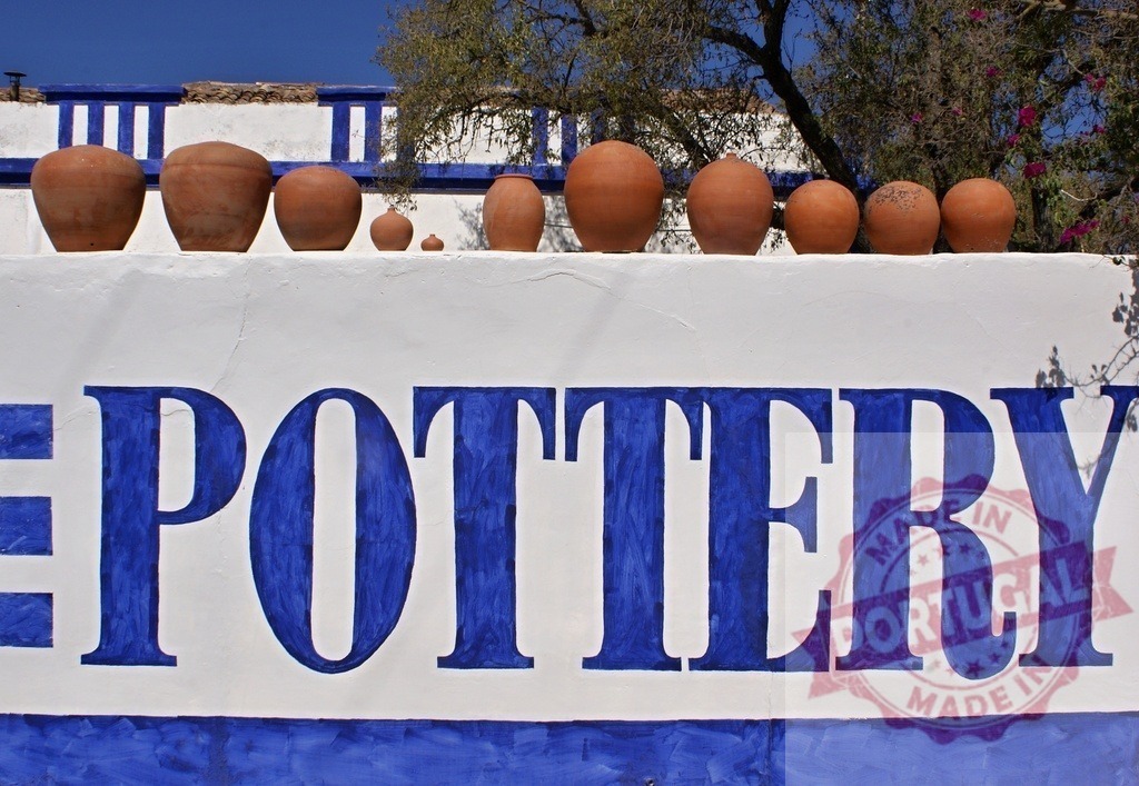 Pottery shop sign displaying terracotta pots outdoors | Pottery shop sign with large blue letters and terracotta pots on a white wall - Realisiert mit Pictrs.com