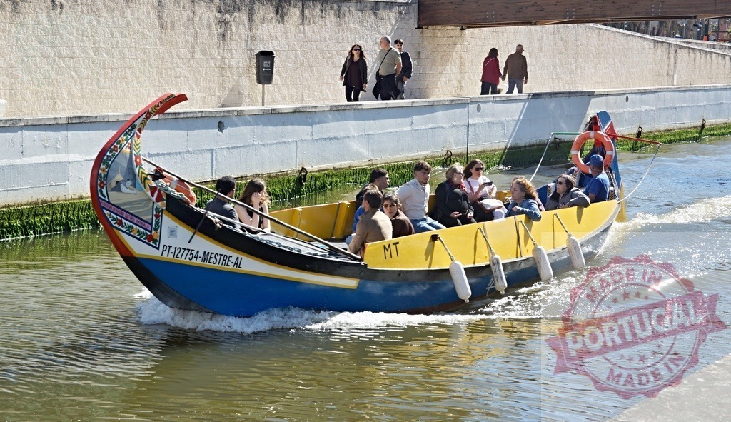 Moliceiro boat carrying tourists on Ria de Aveiro canal. Aveiro - Portugal | Colorful Moliceiro boat transporting tourists along a sunny canal in Aveiro, Portugal - Realized with Pictrs.com