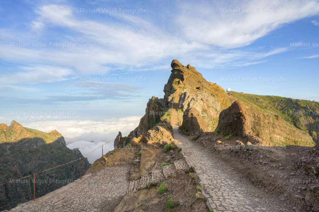 Blick zur Stairway to Heaven und Pico do Arieiro im Hintergrund | Das Bild zeigt einen beeindruckenden Blick auf die Himmelstreppe auf Madeira, mit dem majestätischen Pico do Arieiro im Hintergrund. Die Himmelstreppe ist ein faszinierender Wanderweg, der die Besucher in die atemberaubende Bergwelt der Insel führt. Sie windet sich steil nach oben und gibt den Wanderern das Gefühl, auf den Gipfeln der Welt zu stehen. Umgeben von wilden Felsen und karger Vegetation ist sie eine Herausforderung für alle, die sich auf den Weg machen, aber auch eine Belohnung für diejenigen, die sich der Mühe stellen.Im Hintergrund ragt der Pico do Arieiro, einer der höchsten Berge Madeiras, in den Himmel. Mit einer Höhe von 1.818 Metern bietet der Gipfel bei gutem Wetter einen spektakulären Ausblick über die Insel. - Realisiert mit Pictrs.com