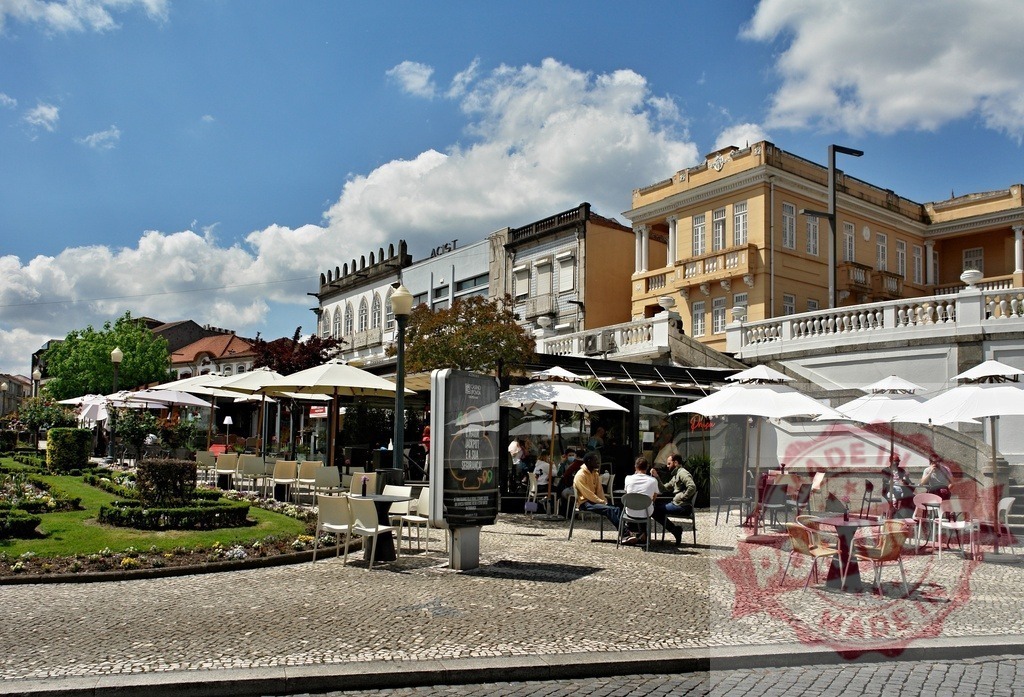 People relaxing at outdoor cafe in Santo Tirso Portugal. Region Norte - Portugal | Outdoor cafe terrace with people, buildings, and garden on a sunny day - Realisiert mit Pictrs.com