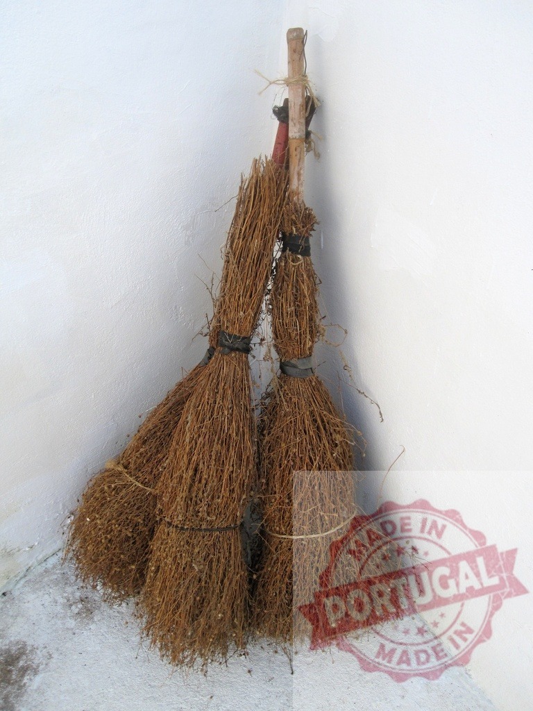 Three traditional straw brooms leaning against white corner wall | Three handmade straw brooms with wooden handles standing in a room corner - Realisiert mit Pictrs.com