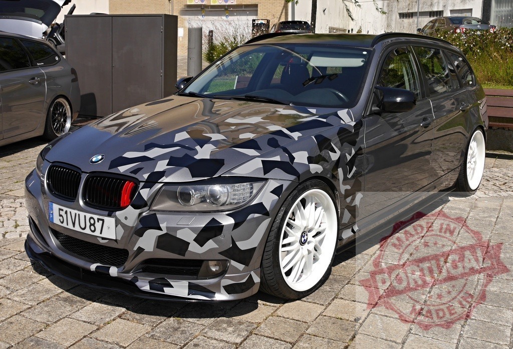 Custom BMW station wagon car with camouflage wrap and white rims | Modified BMW station wagon parked outdoors featuring a custom gray camouflage wrap and white wheels - Realized with Pictrs.com