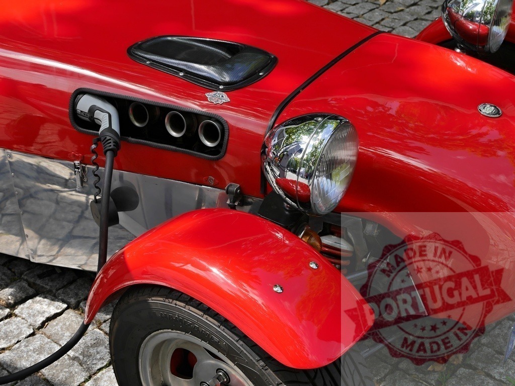 Red electric kit car charging on cobblestone | Red electric kit car plugged in and charging, combining vintage style with modern technology - Realized with Pictrs.com