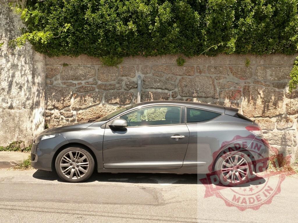Renault Mégane Coupé parked on a sunny street | Grey Renault Mégane Coupé car parked alongside a stone wall and green hedge on a sunny day - Realized with Pictrs.com