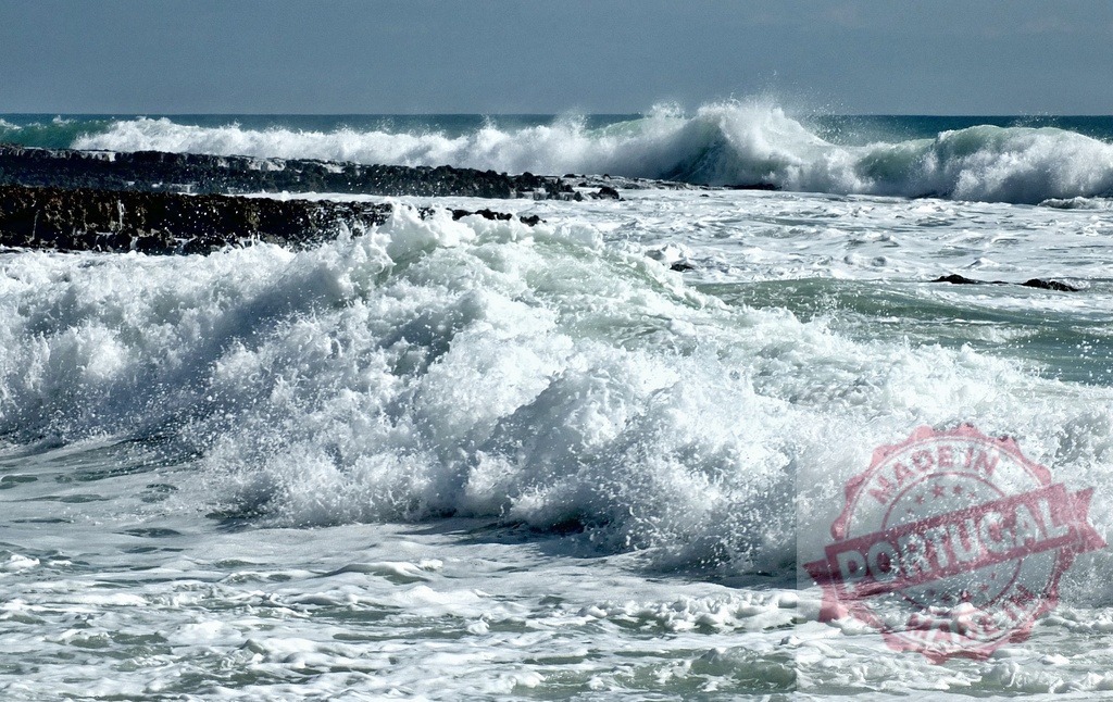 Ocean waves crashing on coastal rocks creating foam | Powerful ocean waves crashing on dark rocks, creating white foam and spray under a bright sky - Realized with Pictrs.com