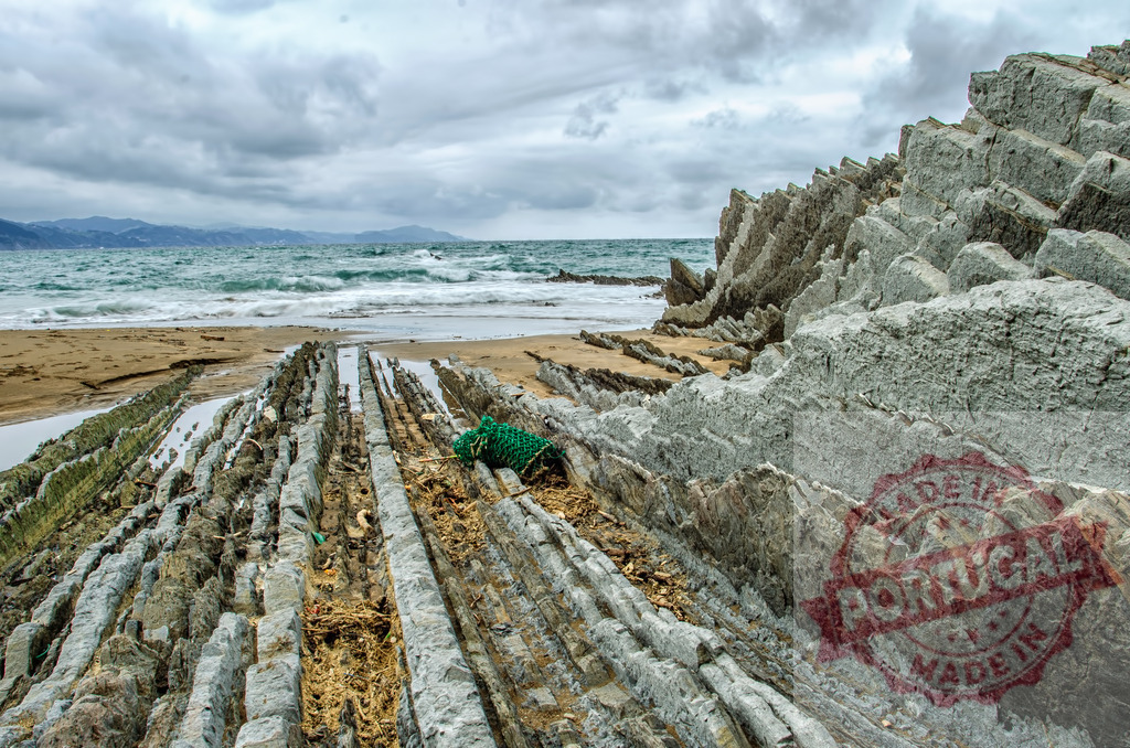 Basque Coast Geopark flysch rock formations beach | Layered flysch rock formations extending into the ocean on a cloudy day at Itzurun beach - Realized with Pictrs.com