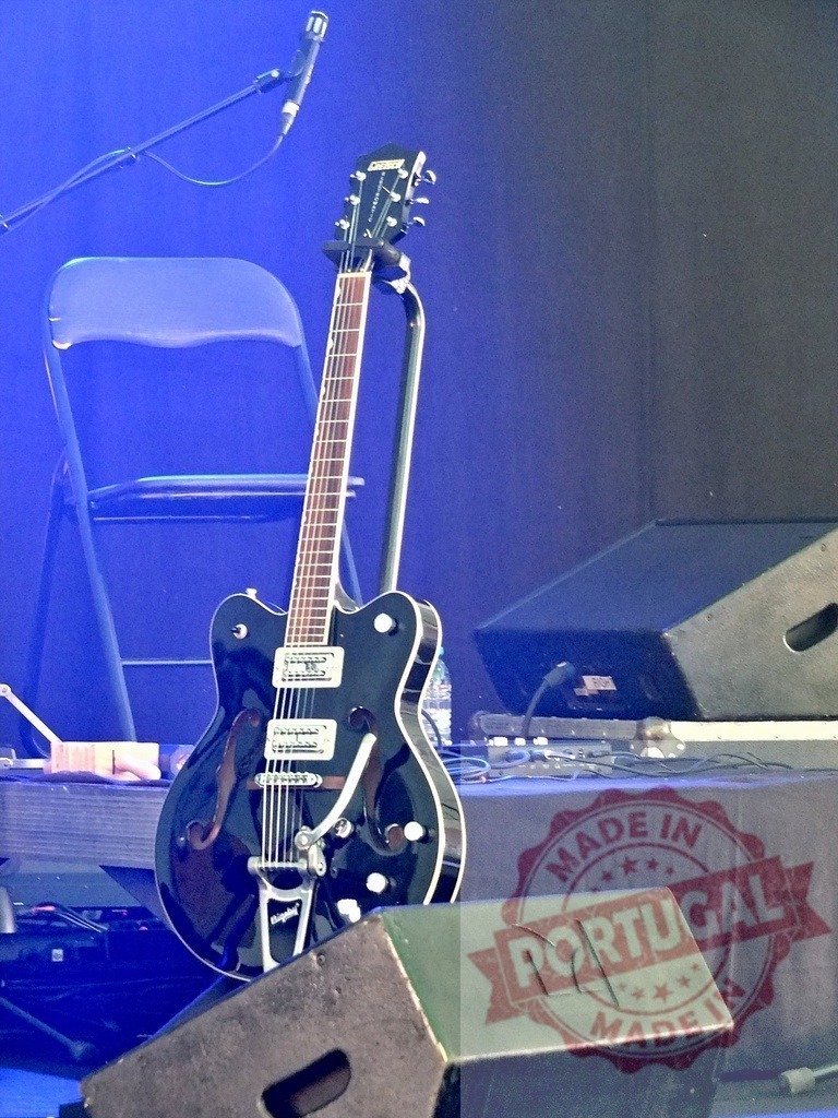 Electric guitar standing on stage ready for the concert | Shiny electric guitar standing on stage next to monitor speakers, ready for a live music performance - Realized with Pictrs.com