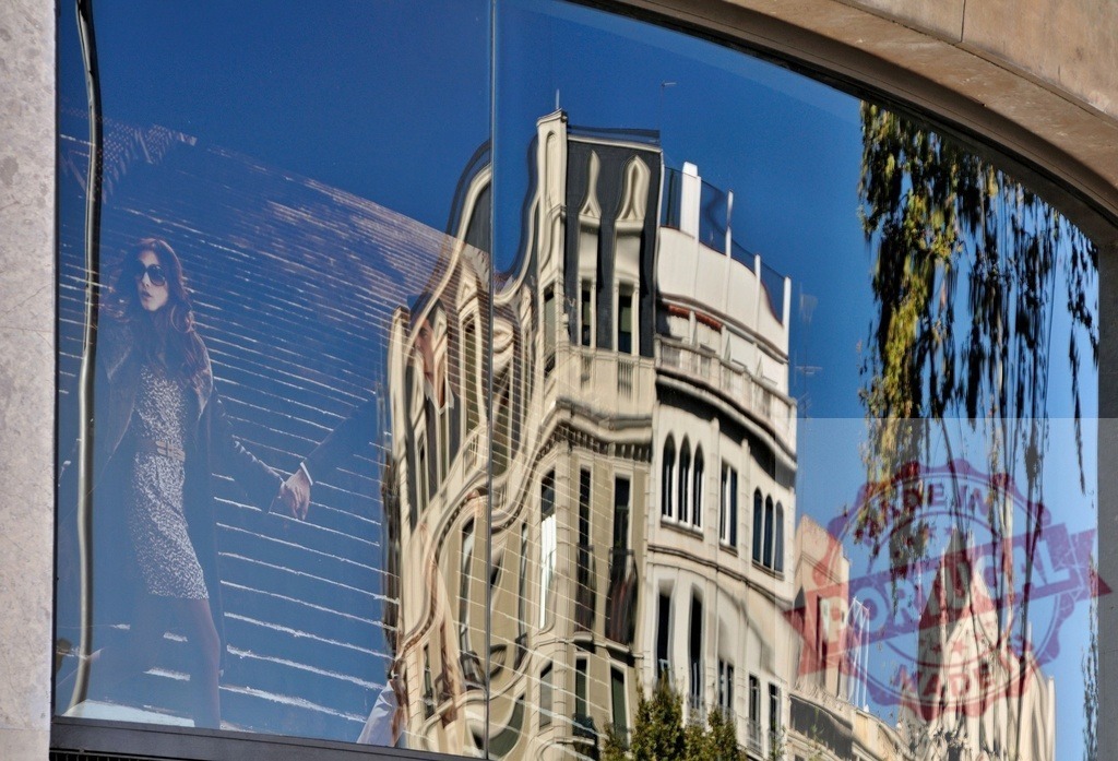 Urban architecture reflecting a female figure in glass. Spain - Barcelona | Distorted city buildings and a female model reflecting in a shop window, abstract urban view - Realized with Pictrs.com