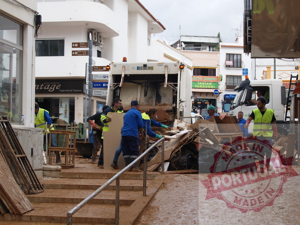 Workers cleaning up flood debris on street | Albufeira Flood - discruction by weather problems People and a garbage truck removing debris and mud after a natural disaster - Realized with Pictrs.com