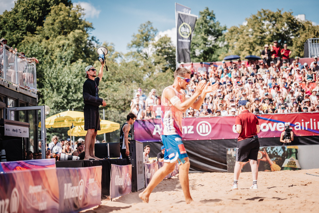 Beachvolleyball | Männer | Allianz German Beach Tour 2025 | Tourstop München | 12.07.2025 | links Bennet Poniewaz mit einem Megafon, während rechts David Poniewaz auf das Feld läuft
