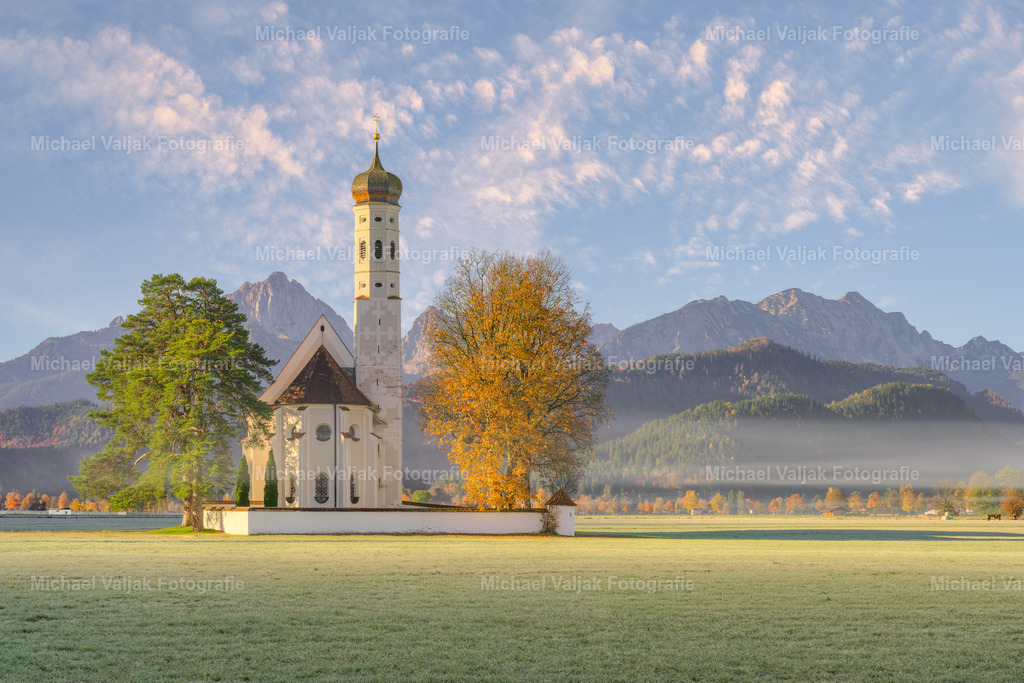 St. Coloman in Schwangau | St. Coloman in Schwangau erstrahlt in der Morgensonne. Leichte Nebelschwaden, die in der Luft liegen, verleihen der Szenerie eine mystische Atmosphäre. Die sanften Strahlen der aufgehenden Sonne tauchen die Landschaft in ein warmes Licht und betonen die majestätische Schönheit der Natur. - Realisiert mit Pictrs.com