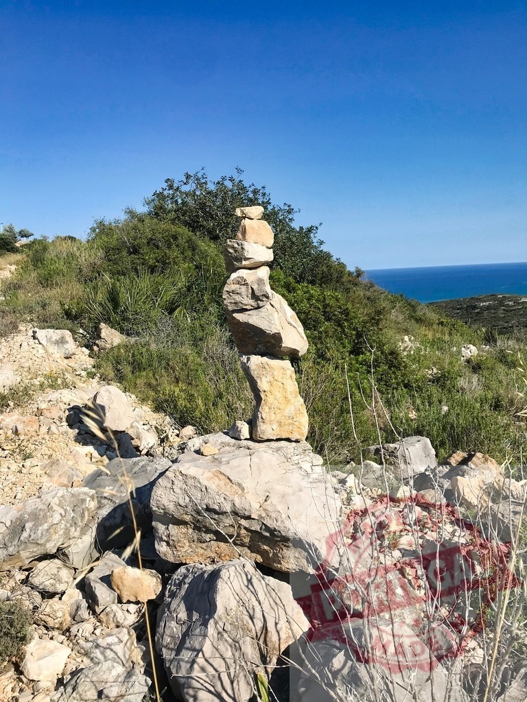 Balancing stones cairn on coastal hill with Mediterranean sea | Stacked rocks forming a cairn on a rocky hillside overlooking the clear blue sea - Realized with Pictrs.com
