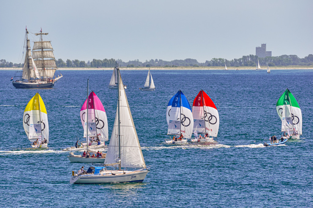 Segelboot-Regatta | Farbenprächtige Segelboote bei einer Regatta zur Kieler Woche. Die Aufnahme entstand in Höhe von Kiel-Schilksee, im Hintergrund fahren die niederländische Brigg Mercedes und Boote mit Zuschauern. — Auflösung des Originals: 5946 x 3964 px. - Realisiert mit Pictrs.com