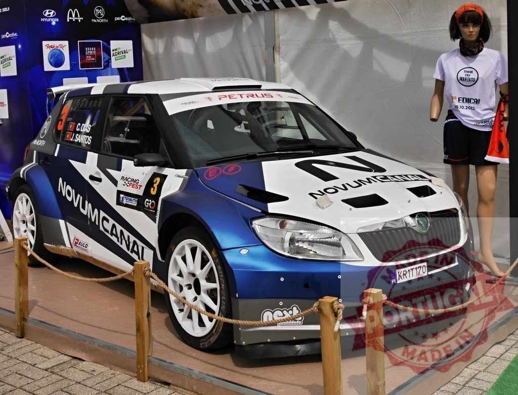 Škoda Fabia rally car at motorsports exhibition | Škoda Fabia rally car on display with sponsor logos and a mannequin wearing race gear - Realisiert mit Pictrs.com