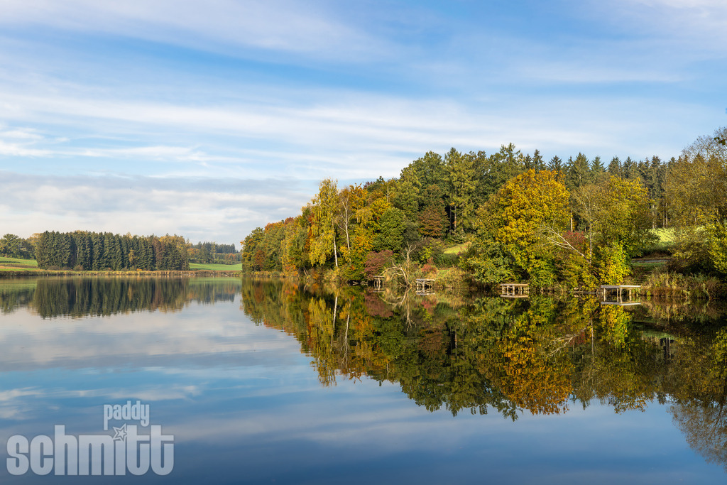 Lausheimer Weiher bei Ostrach im Herbst | Der Lausheimer Weiher bei Ostrach zeigt sich im Herbst von seiner besonders stimmungsvollen Seite. Bunte Bäume spiegeln sich im ruhigen Wasser, während das warme Herbstlicht die idyllische Landschaft in leuchtende Farben taucht. - Realisiert mit Pictrs.com