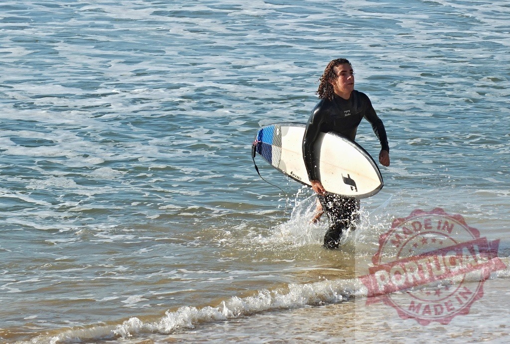 Young surfer running into ocean with board | Young man wearing a wetsuit running through shallow water carrying a surfboard - Realized with Pictrs.com