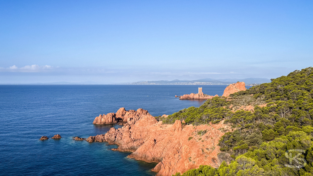 Rote Felsen des Esterel-Gebirges am Cap Dramont – Côte d’Azur | Panorama-Aufnahme der markanten roten Felsküste des Massif de l’Esterel am Cap Dramont mit Blick auf das tiefblaue Mittelmeer und die Île d’Or unter strahlend blauem Himmel. - Realisiert mit Pictrs.com