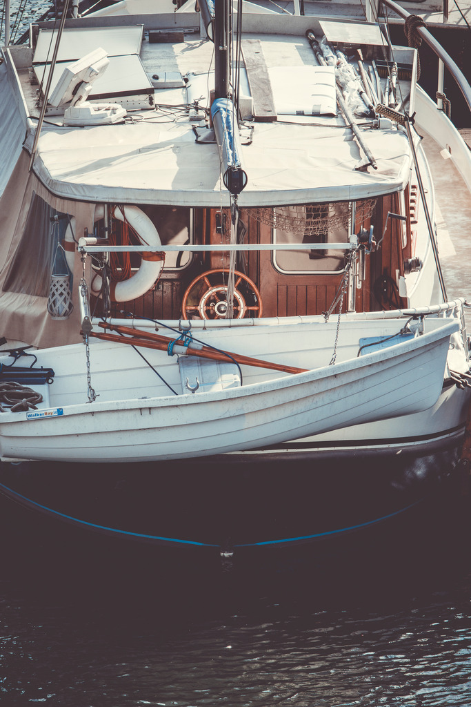 Harbor Stories | Ein klassisches Boot liegt ruhig im Hafen, umgeben von Holz, Tauwerk und den Spuren vieler Jahre auf dem Wasser.Das kleine Beiboot, das hölzerne Steuerrad und die sichtbaren Gebrauchsspuren verleihen der Szene einen nostalgischen, fast zeitlosen Charakter. Die zurückhaltenden Farben und die warme, leicht entsättigte Bearbeitung unterstreichen die ruhige maritime Atmosphäre.Ein Fine-Art-Motiv über Handwerk, Reisen und die Geschichten, die alte Boote über die Jahre sammeln. - Realisiert mit Pictrs.com