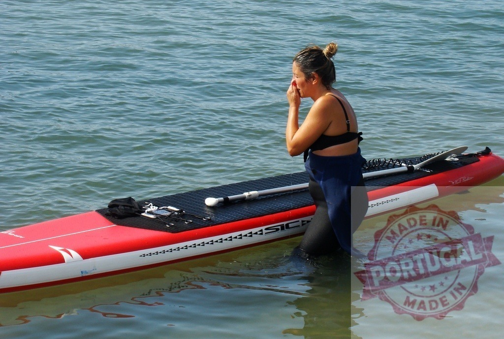 Woman preparing to paddleboard in ocean water | Woman standing in ocean water next to a paddleboard, adjusting her wetsuit ready for watersports - Realisiert mit Pictrs.com
