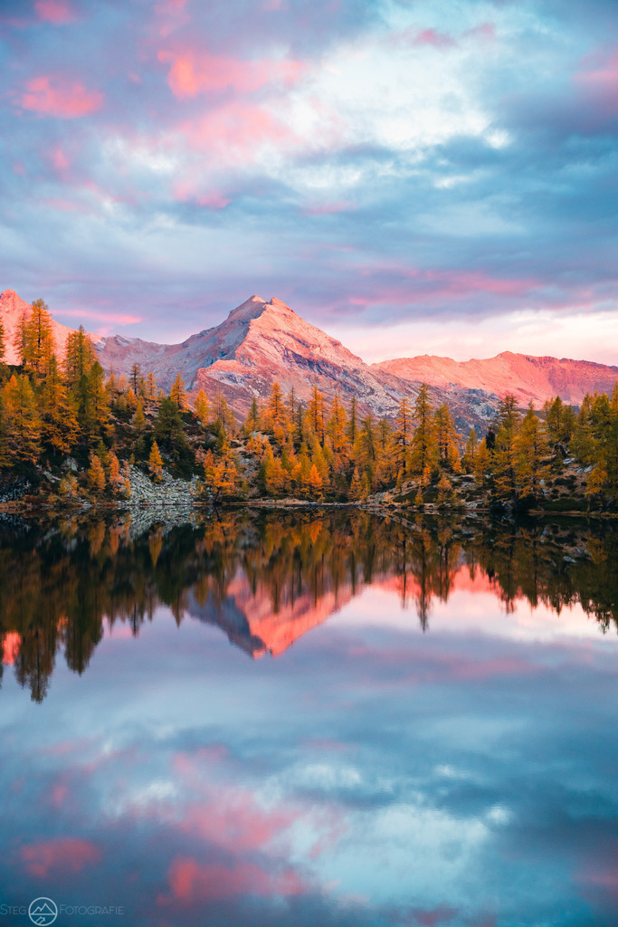 Morgen im Valle di Campo, TI | Herbststimmung in einem Tal im Tessin. Vom Sonnenaufgang erhellte Wolken spiegeln sich in einem Bergsee.Format 3 zu 2 - Realisiert mit Pictrs.com