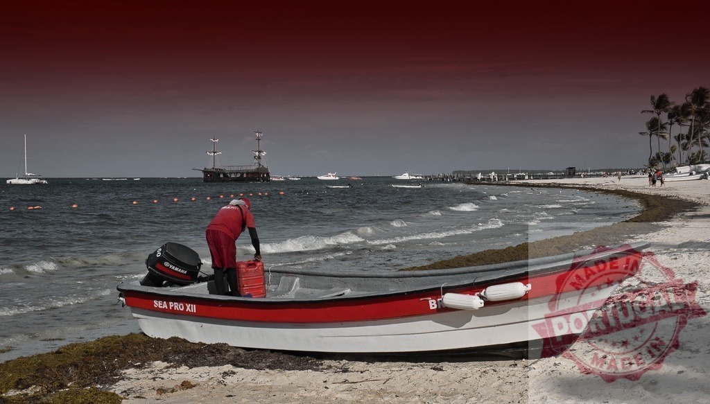 Man fueling boat on Caribbean beach with sargassum | Man fueling red boat on a tropical beach with a pirate ship and palms in the distance - Realisiert mit Pictrs.com