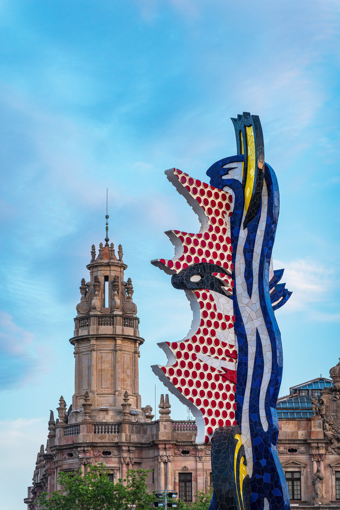 Die Skulptur La Cara de Barcelona und ein historischer Turm in Barcelona, Spanien | Die Skulptur La Cara de Barcelona und ein historischer Turm in Barcelona, Spanien.           