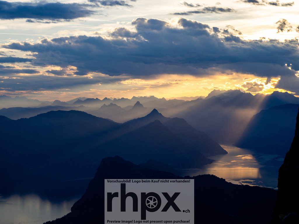 Lichtdurchflutete Gipfel | <p><strong>Licht. Weite. Magie.</strong></p><p>Dramatische Sonnenstrahlen durchbrechen die Wolkendecke und tauchen die gestaffelten Bergketten in ein atmosphärisches, goldenes Licht. Dieser Moment fängt die pure Erhabenheit der Alpen in einer einzigartigen Lichtstimmung ein.</p><p>Wähle unter "Produktauswahl" dein Wunschformat: Vom klassischen Wandbild über Puzzle & Tassen bis zum digitalen Download (z.B. als Handy-Hintergrund).</p> - Realisiert mit Pictrs.com