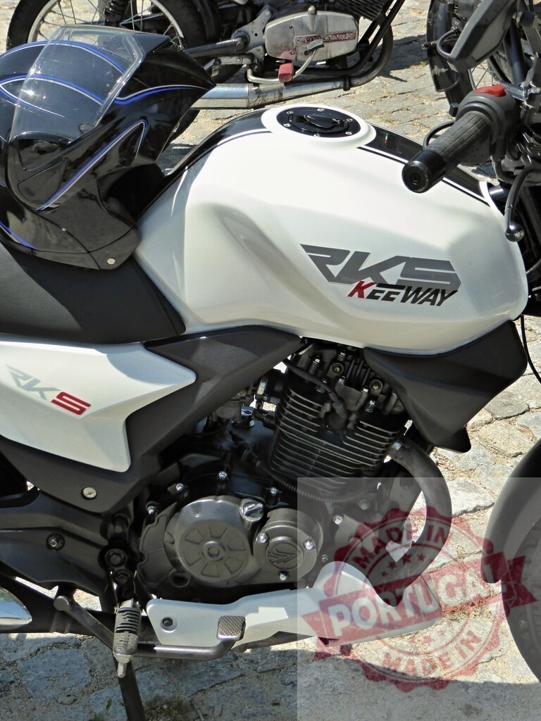 Keeway RKS 125 motorcycle parked on cobblestone street with helmet resting on seat | Close-up of a white and black Keeway RKS 125 motorcycle with a helmet on the seat, parked on a cobblestone street - Realized with Pictrs.com