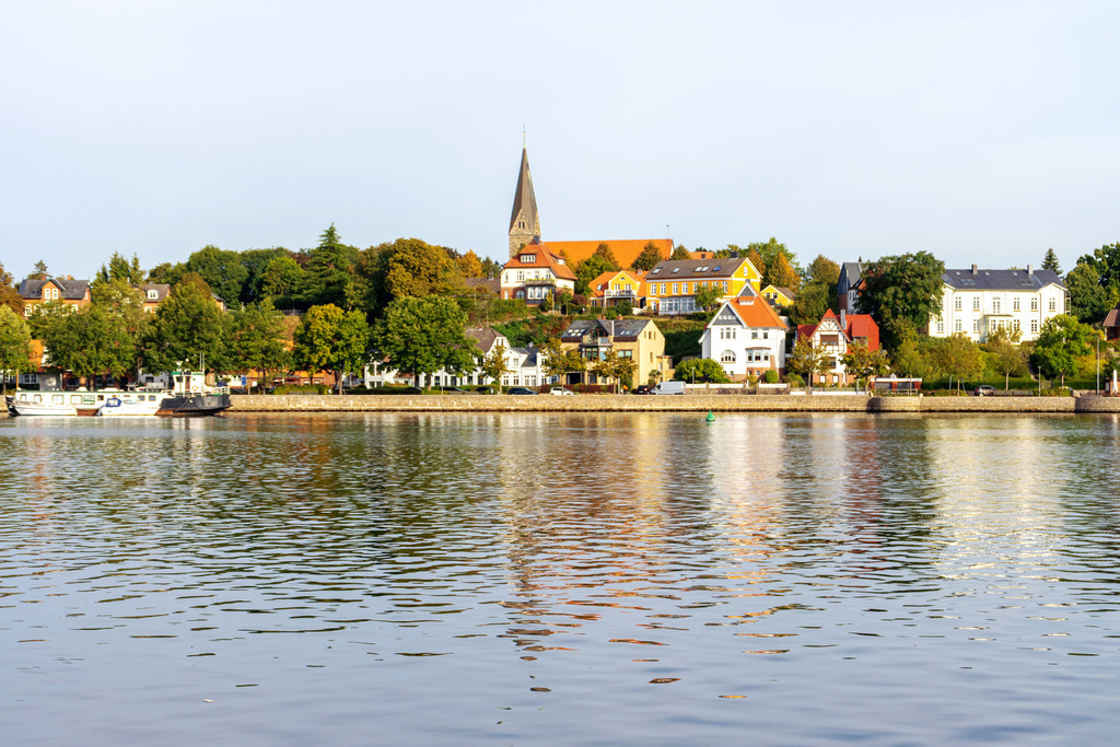 Wandbild: Hafen in Eckernförde mit Blick zur Kirche in Borby | Dieses Wandbild im Querformat zeigt den Hafen in Eckernförde mit Blick zur Kirche in Borby. Auf dem Wasser ist eine schöne Spiegelung zu sehen. Der blaue Himmel ist fast wolkenlos - Realisiert mit Pictrs.com