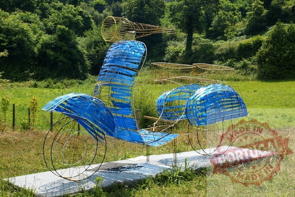 Blue wireframe scooter sculpture in outdoor art installation | Large blue and yellow wire scooter sculpture standing on a concrete base in a green park - Realisiert mit Pictrs.com