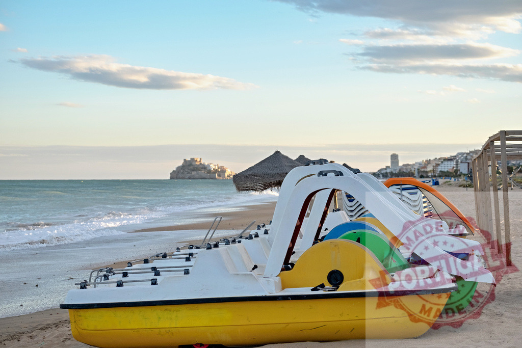 Colorful pedal boats lining Peniscola beach at sunset | Colorful paddle boats resting on a sandy beach with the sea and Peniscola Castle in the background - Realisiert mit Pictrs.com