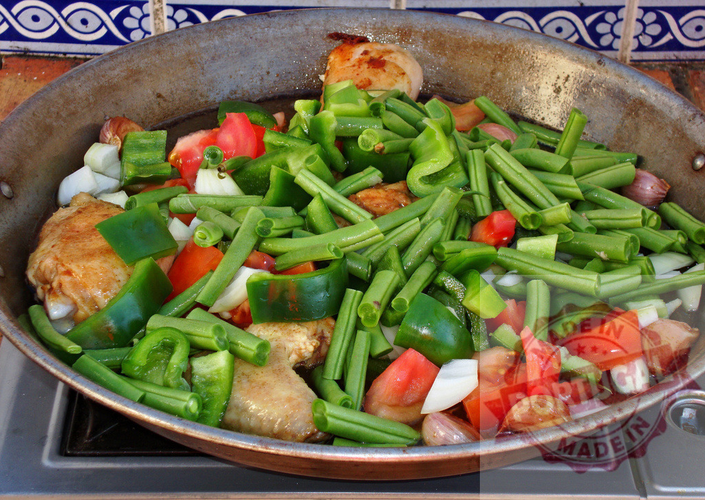Cooking paella with chicken and fresh vegetables | Chicken and chopped vegetables cooking in a traditional paella pan on a stove - Realized with Pictrs.com