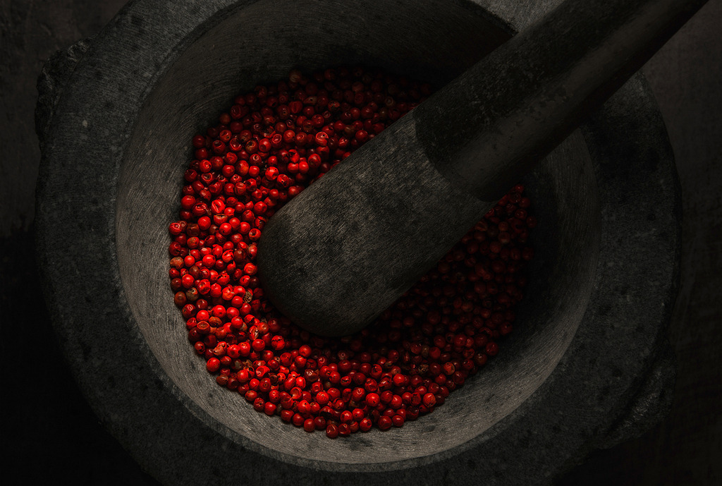 tempation in red | Rote Pfefferkörner in einem dunklen Steinmörser mit Stößel. Dramatisches Licht betont das leuchtende Rot und die raue Struktur des Steins. - Realisiert mit Pictrs.com