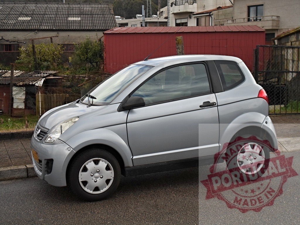 Silver microcar parked on urban street | Silver microcar parked on asphalt road in front of old buildings with a red shed - Realized with Pictrs.com