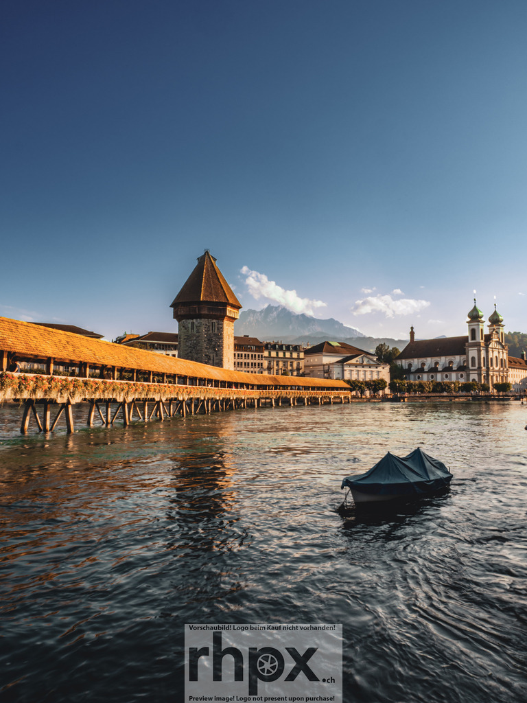 Kapellbrücke Luzern mit Pilatus im Hintergrund | Brücke. Himmel. Klarheit.Die Kapellbrücke und der Wasserturm erstrahlen unter einem weiten, blauen Himmel. Im Hintergrund erhebt sich das eindrucksvolle Bergpanorama der Zentralschweiz, während rechts die barocke Jesuitenkirche das Uferbild ergänzt. Ein kleines, vertäutes Boot ruht im Vordergrund.Wähle unter "Produktauswahl" dein Wunschformat: Vom klassischen Wandbild über Puzzle &amp; Tassen bis zum digitalen Download (z.B. als Handy-Hintergrund). - Realisiert mit Pictrs.com