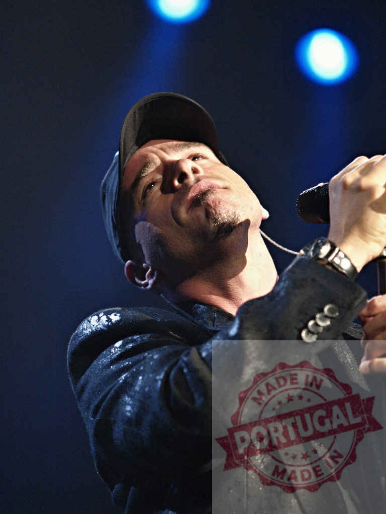 Singer performing live on stage, holding microphone and wearing baseball cap | Male singer emotionally singing into microphone during live concert performance, wearing baseball cap and black jacket - Realized with Pictrs.com