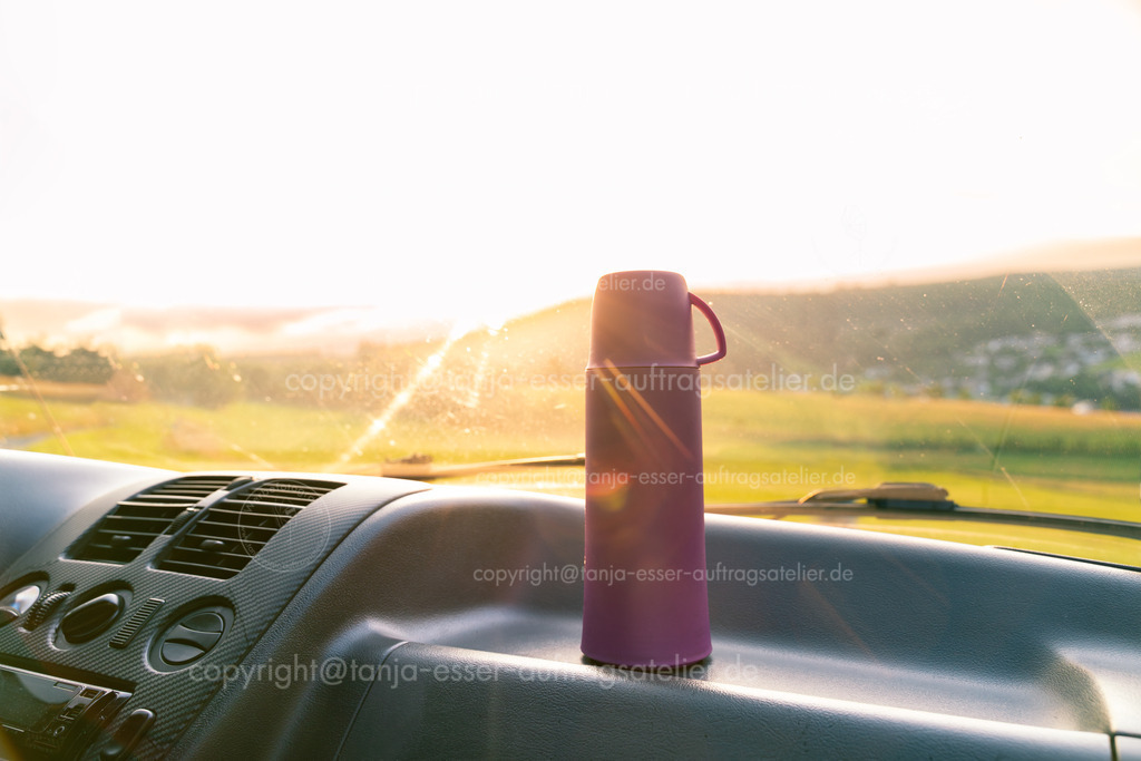 Thermoskanne im Van, durch die Windschutzscheibe sieht man den Sonnenuntergang in Willingen | Vanlife. Eine Thermoskanne steht im Fahrerhaus eines Van. Der Van parkt mit schöner Aussicht in Willingen Upland in Deutschland. Stimmungsvolle Nahaufnahme mit Sonnenuntergang. 
