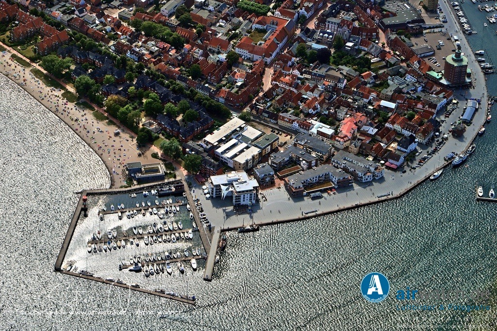 Luftbild Eckernförde - Die Stadt erlebte erhebliche Schäden durch Naturkatastrophen | Die Stadt erlebte erhebliche Schäden durch Naturkatastrophen, darunter eine Sturmflut 1872, die 122 Häuser zerstörte und 400 Menschen obdachlos machte, sowie eine weitere Sturmflut am 20. Oktober 2023, die Strand, Dünen und Promenade schwer beschädigte. Eckernförde erhielt 1986 die Auszeichnung „UNO-Stadt“ und ist heute ein bekanntes Ostseebad mit einem modernen Meerwasser Wellenbad, das 2012 umfassend saniert wurde.