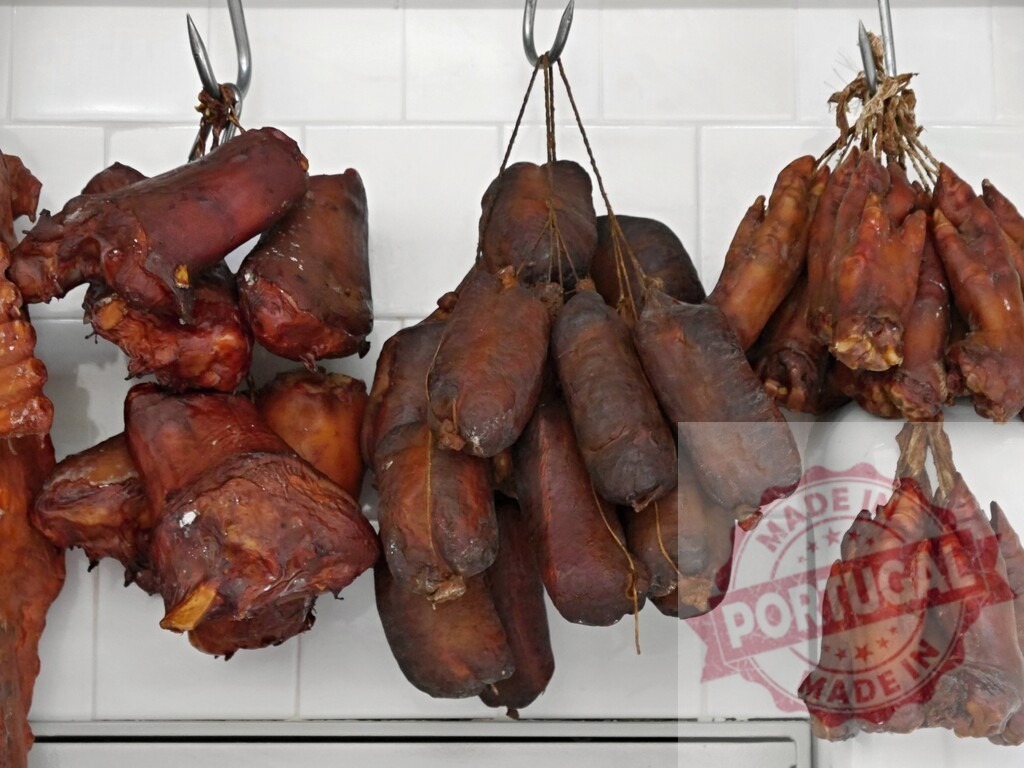 Smoked pork trotters and sausages hanging in butcher shop | Smoked pork meat products hanging on hooks inside a butcher shop - Realized with Pictrs.com