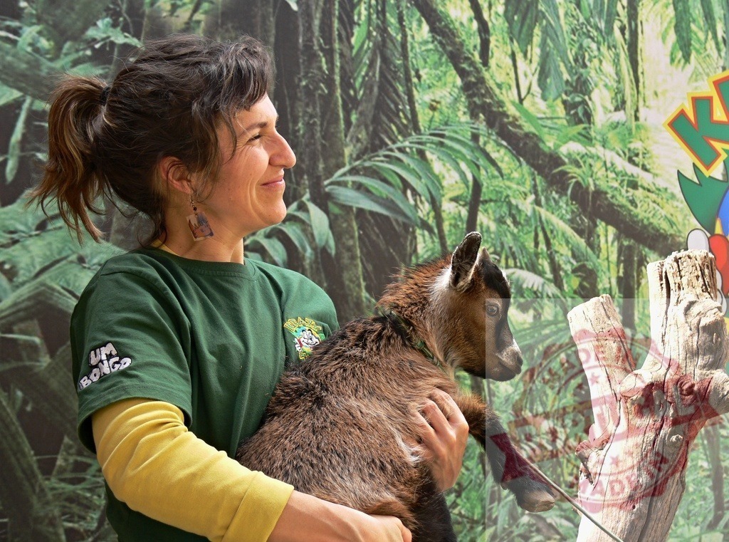 Zookeeper woman holding a baby goat kid smiling | Zookeeper woman holding a cute baby goat kid in hands, showing animal care - Realized with Pictrs.com