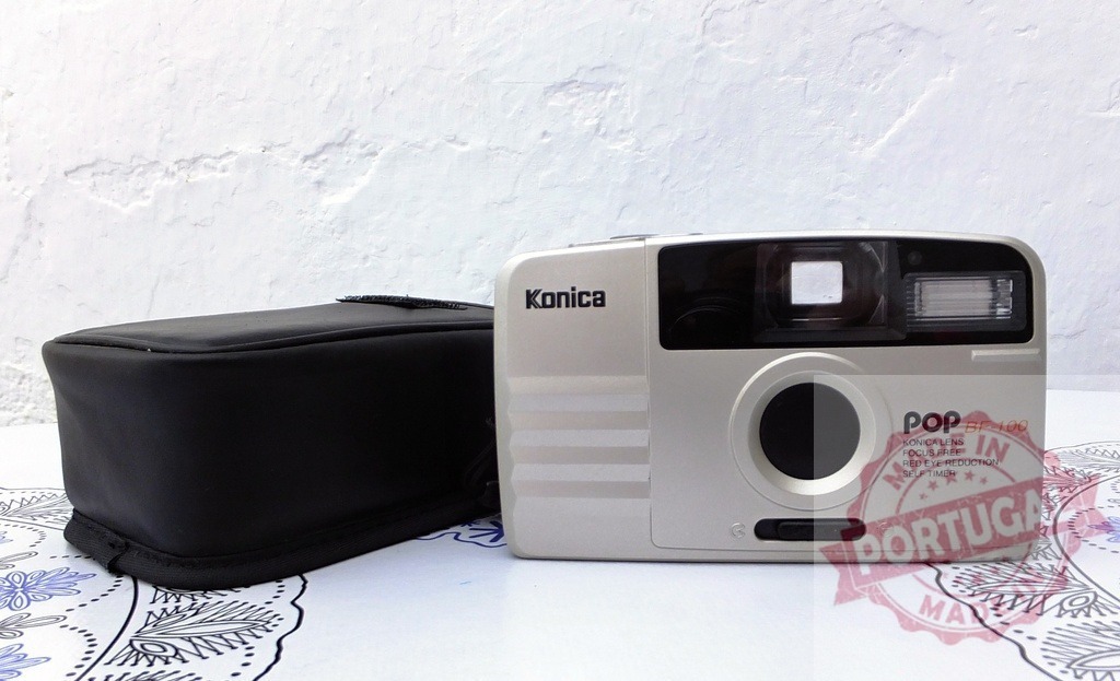 Konica Pop BF-100 film camera with black case | Konica Pop BF-100 point and shoot film camera with its black carrying pouch, resting on a patterned surface - Realisiert mit Pictrs.com
