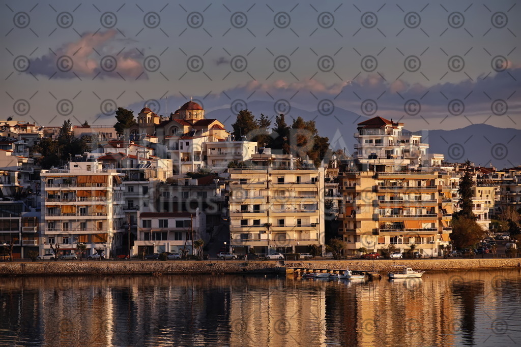 Die Skyline von Chalkida | Die Skyline der Festlandseite von Chalkida (Χαλκίδα). Chalkida ist die Hauptstadt der der griechischen Insel Euböa (Εύβοια). Chalkida erstreckt sich über beide Seiten der Meeresstraße Euripos (Εύριπος), welche zwischen dem griechischen Festland und der Insel Euböa liegt. 
Über den Dächern der Promenade ragt die Kuppe der griechisch-orthodoxen Kirche "Ekklisia Evaggelismos Theotokou" (Εκκλησία Ευαγγελισμός Θεοτόκου). Im Vordergrund spiegelt sich die Skyline im Morgenlicht in der Meeresenge von Euripos. Die Meerenge ist an der engsten Stelle nur 40 Meter breit und gilt als schmalste Meerenge der Welt. Eine Besonderheit der Meerenge sind die wechselnden Gezeitenströmungen. Die regulären Gezeitenströmungen wechseln alle 6 Stunden die Richtung. Zwei mal pro Mondmonat treten die irregulären Strömungen auf, die bis zu vierzehn mal am Tag die Richtung wechseln.