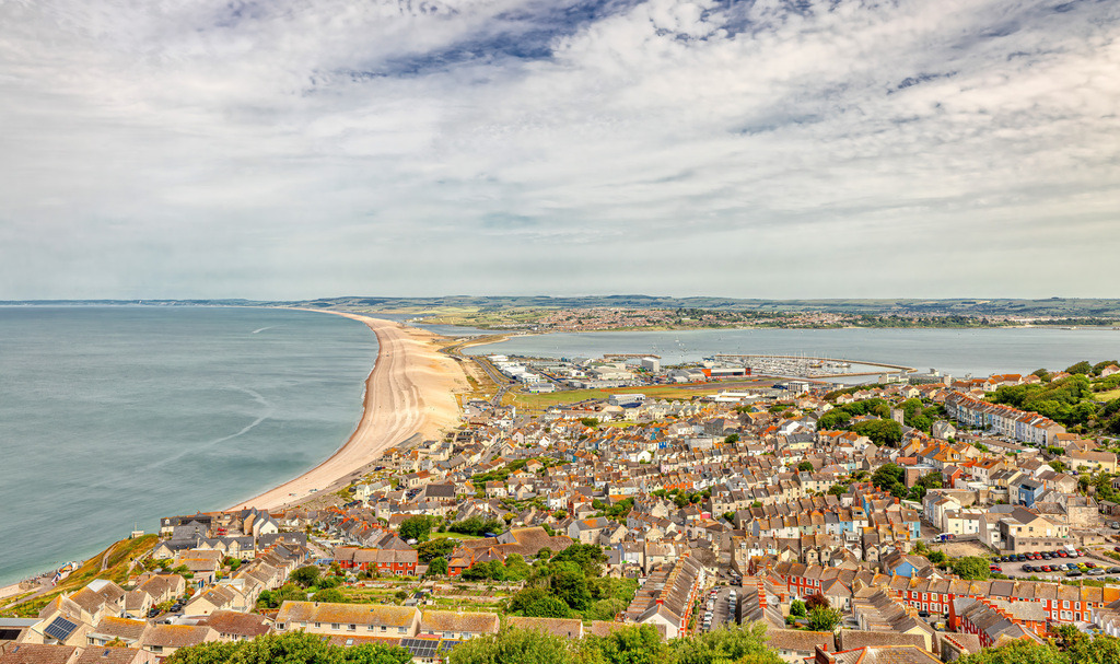 Die Insel Portland und der Chesil Beach----UNESCO Welterbe | Dieses Bild zeigt den Chesil Beach, einen berühmten 18 Meilen langen Kiesstrand in Dorset, England.Im Vordergrund ist der Ort Fortuneswell auf der Isle of Portland zu sehen, von wo aus dieser Blick aufgenommen wurde.Im Hintergrund erstreckt sich die Stadt Weymouth entlang der Küste.Die Isle of Portland ist durch diesen natürlichen Damm mit dem Festland verbunden und bekannt für ihren Kalkstein. - Realisiert mit Pictrs.com