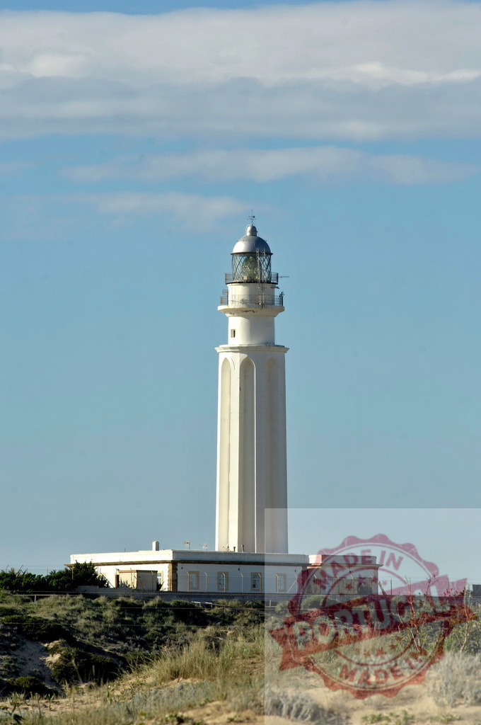Faro de Cabo Trafalgar white lighthouse standing on grassy dune. Espana - Cadiz | Faro de Cabo Trafalgar lighthouse guiding ships on the Cadiz coast - Realized with Pictrs.com
