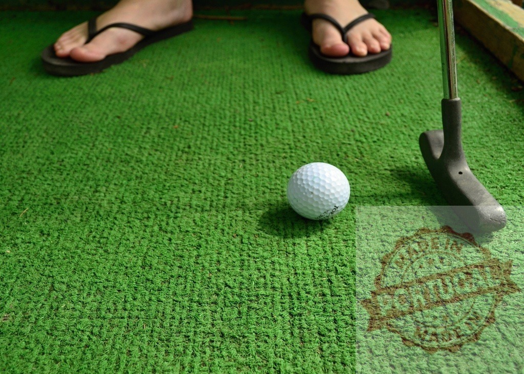 Player aiming golf ball on mini golf green with putter | Golfer putting golf ball on mini golf green with putter - Realisiert mit Pictrs.com