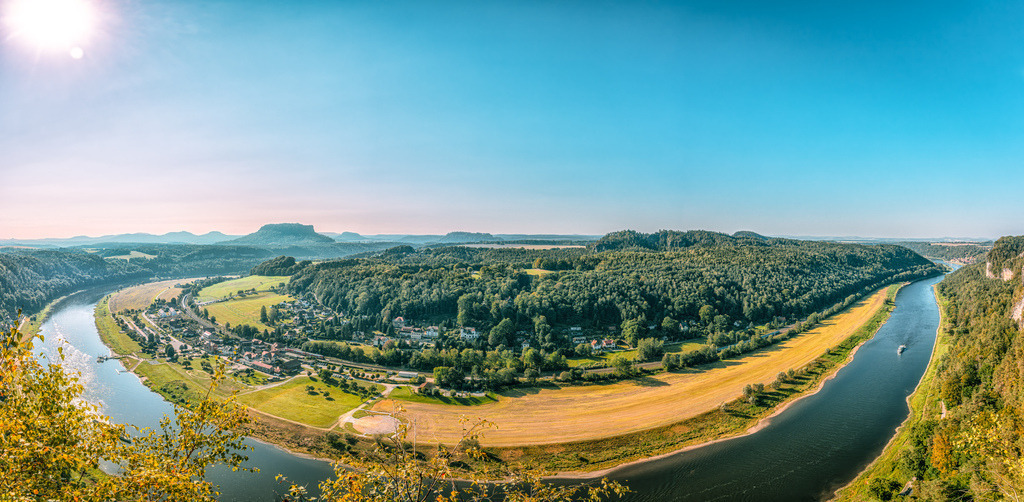 Panoramaansicht des Elbtals in der Sächsischen Schweiz | Das Bild zeigt eine panoramische Ansicht des Elbtals im Nationalpark Sächsische Schweiz in Sachsen.Im Vordergrund windet sich die Elbe durch die Landschaft, mit der Stadt Wehlen oder Rathen am Ufer.Im Hintergrund sind die charakteristischen Tafelberge und Felsformationen des Elbsandsteingebirges zu sehen.Die Region ist bekannt als beliebtes Ziel für Wanderungen auf dem Malerweg - Realisiert mit Pictrs.com